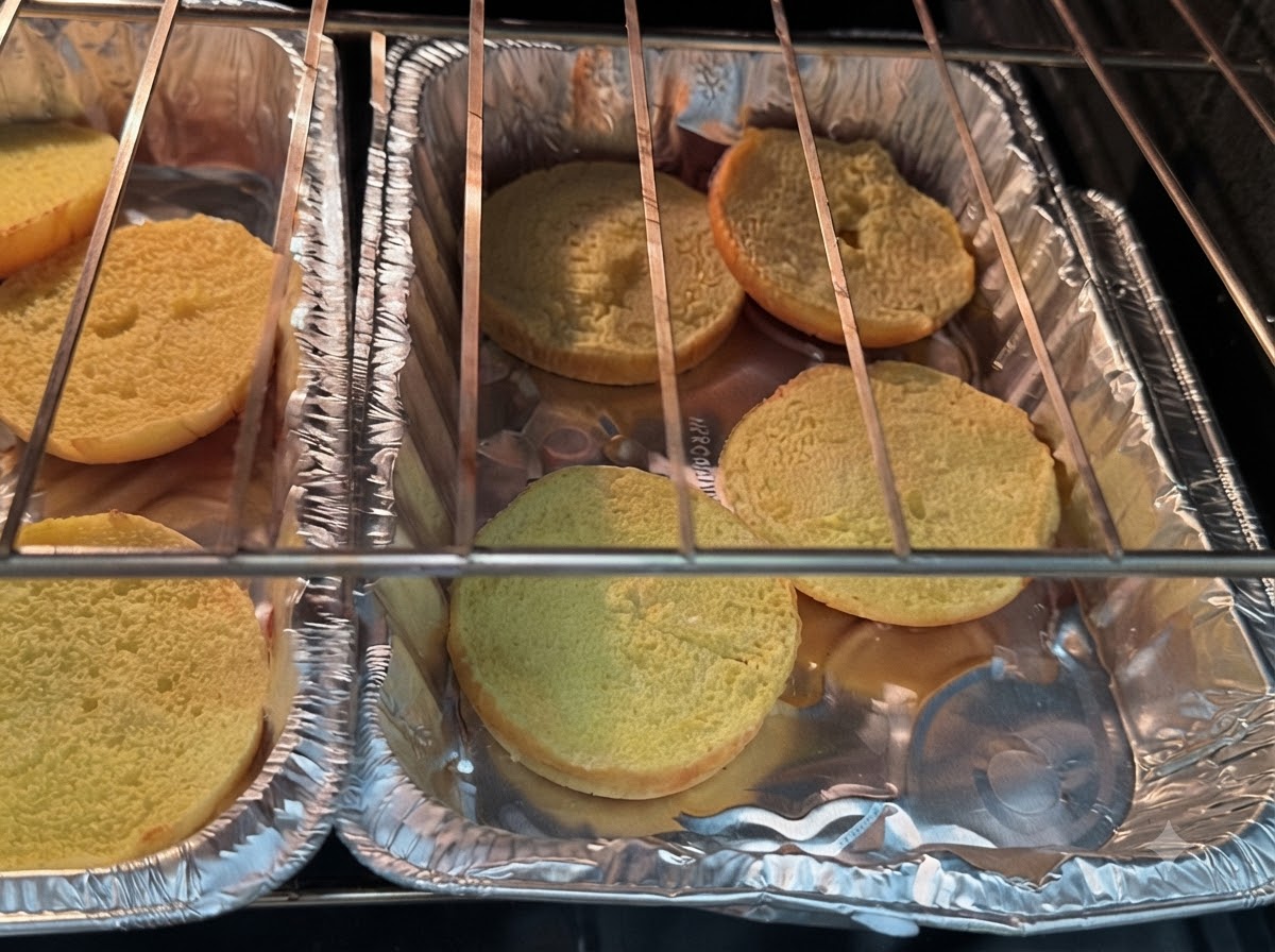 Burgerbrötchen-Hälften liegen auf Alufolie unter den Heizspiralen des Ofens.