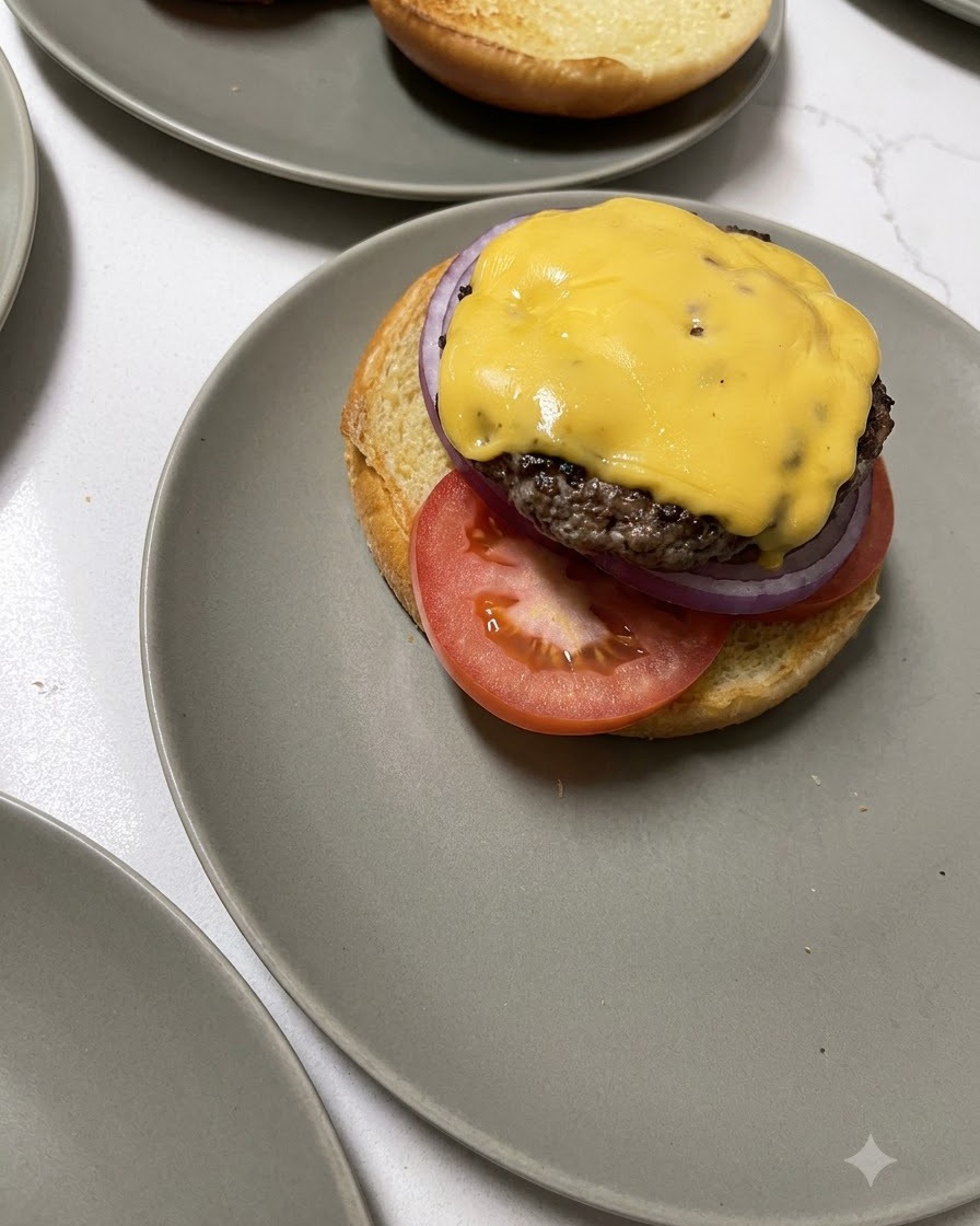 Ein mit Käse überbackenes Rindfleisch-Patty wird mit einem Holzpfannenwender auf die untere Brötchenhälfte gelegt.