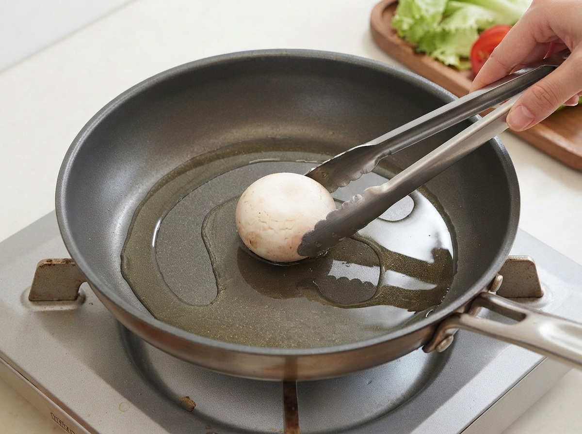 Ein einzelner Pilz wird mit einer Zange in eine geölte Bratpfanne gelegt.