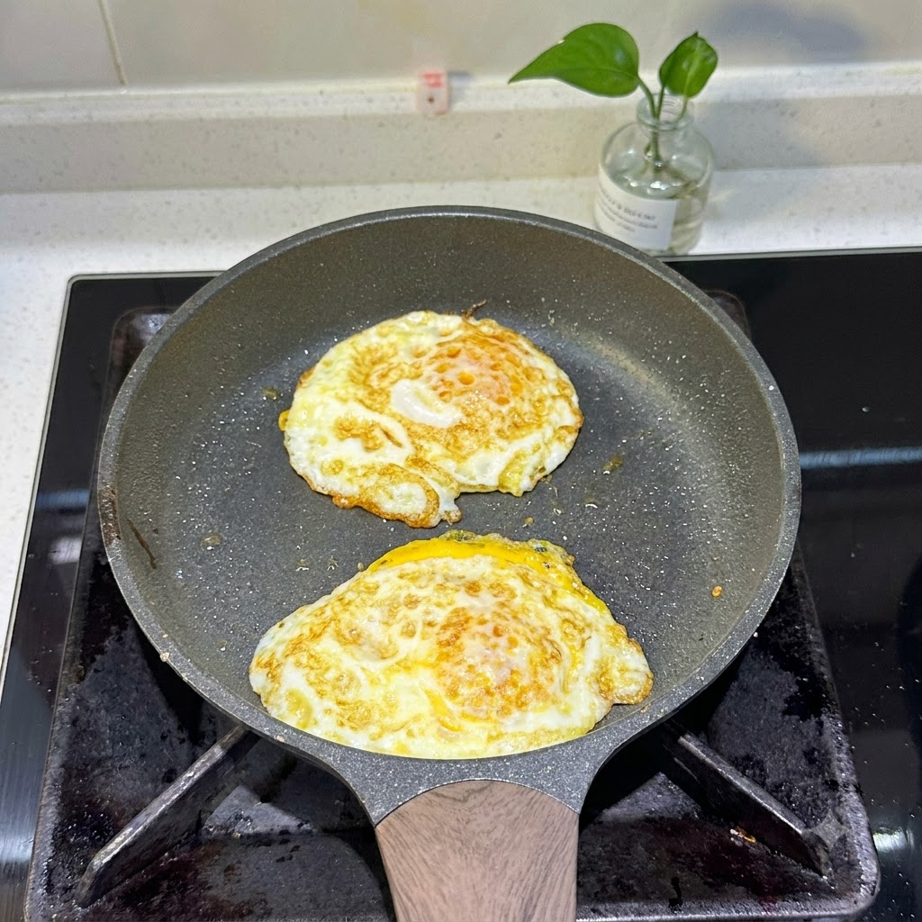Zwei Spiegeleier braten in einer Pfanne mit goldbraunen Rändern.