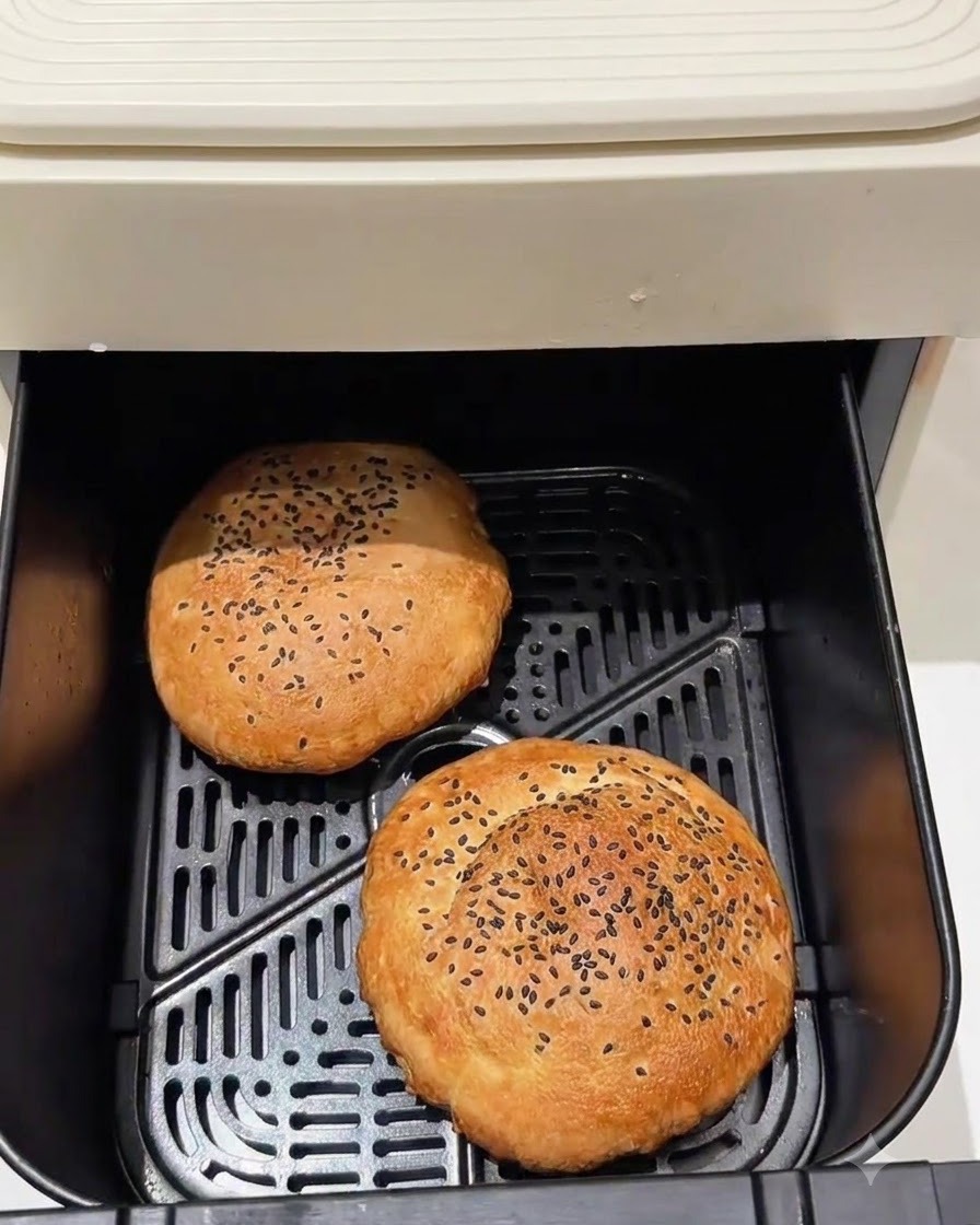 Gebackene Burgerbrötchen liegen im Korb eines Air Fryers.