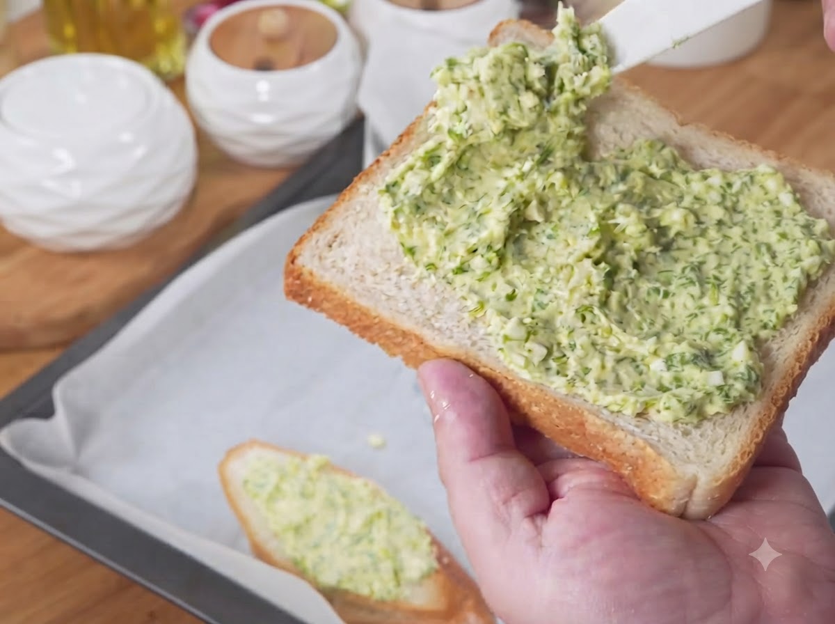 Brotscheiben mit grüner Knoblauchbuttermischung auf einem mit Backpapier ausgelegten Backblech angeordnet.