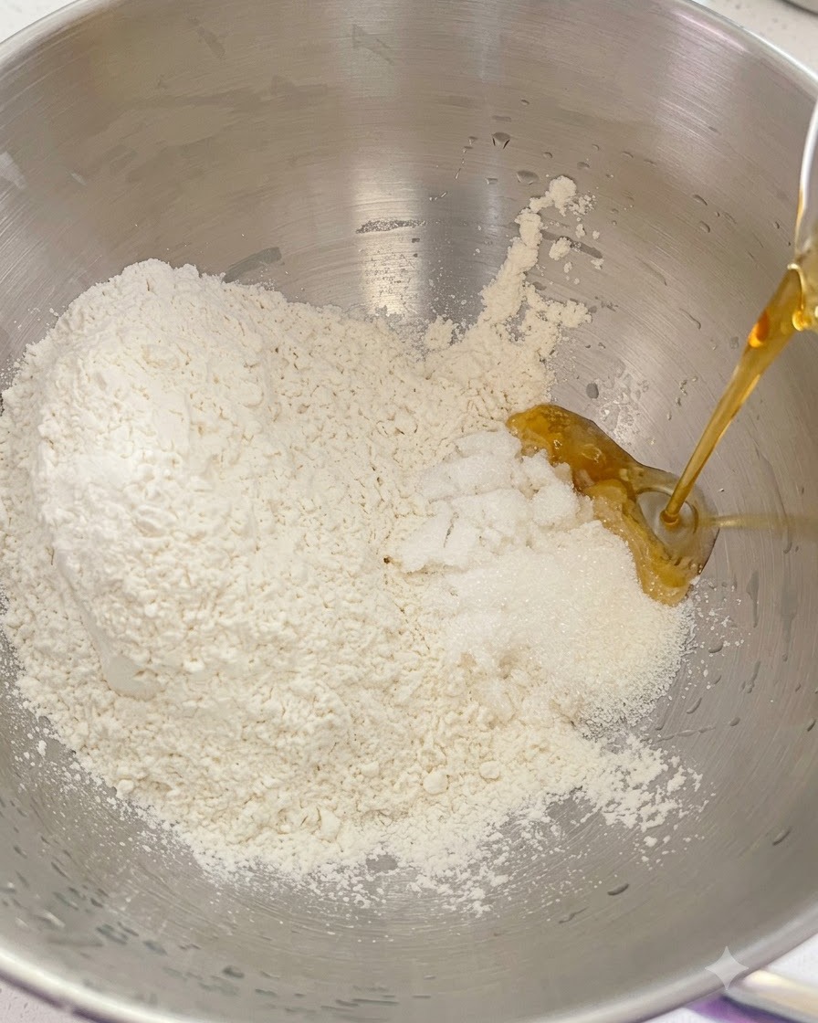Trockenmehl, Zucker und flüssige Zutaten werden gemeinsam in eine Metallschüssel der Küchenmaschine gefüllt.