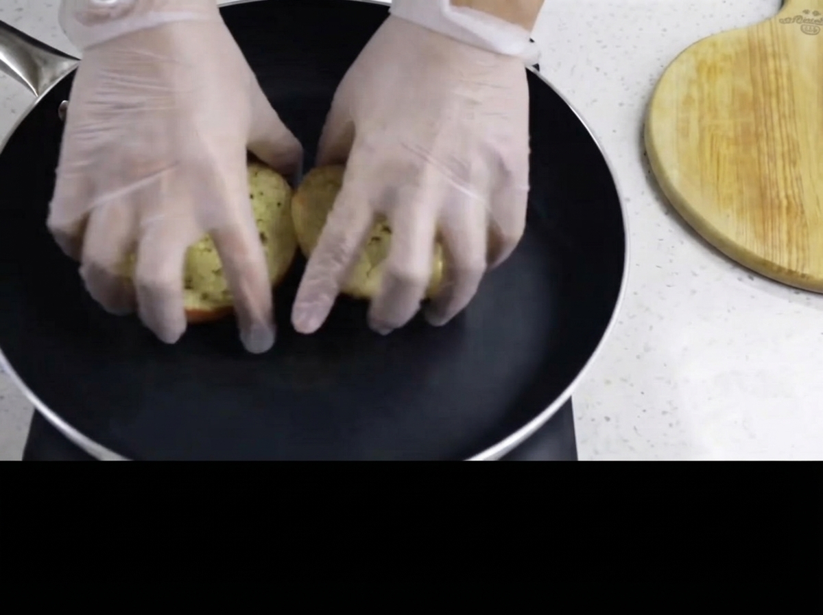 Hände legen die butterbestrichenen Burgerbrötchen mit der Innenseite nach unten in eine heiße Bratpfanne.