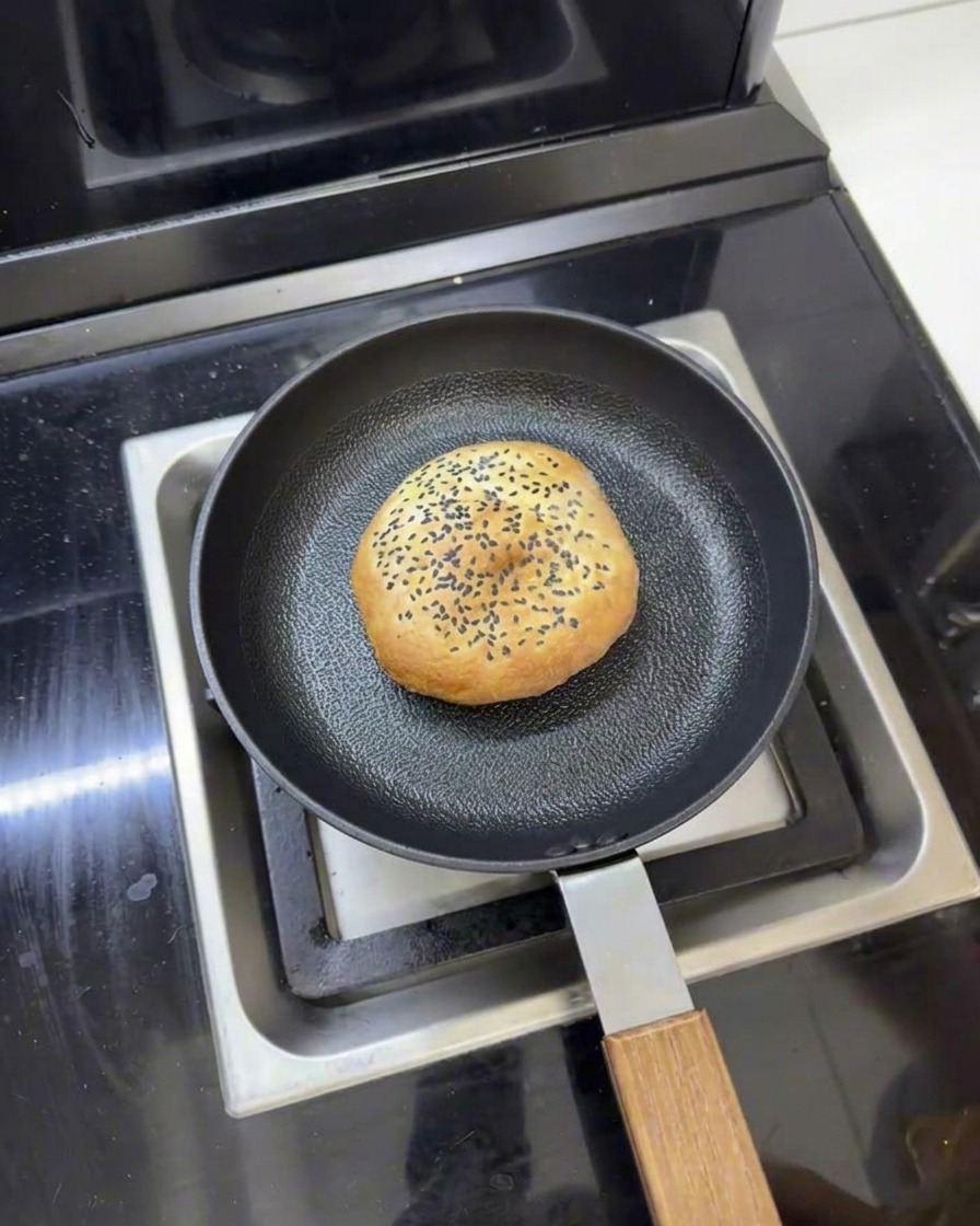 Ein Butter-Burger-Brötchen in einer Pfanne mit etwas Wasser um sich herum, bereit zum Dämpfen mit Deckel.