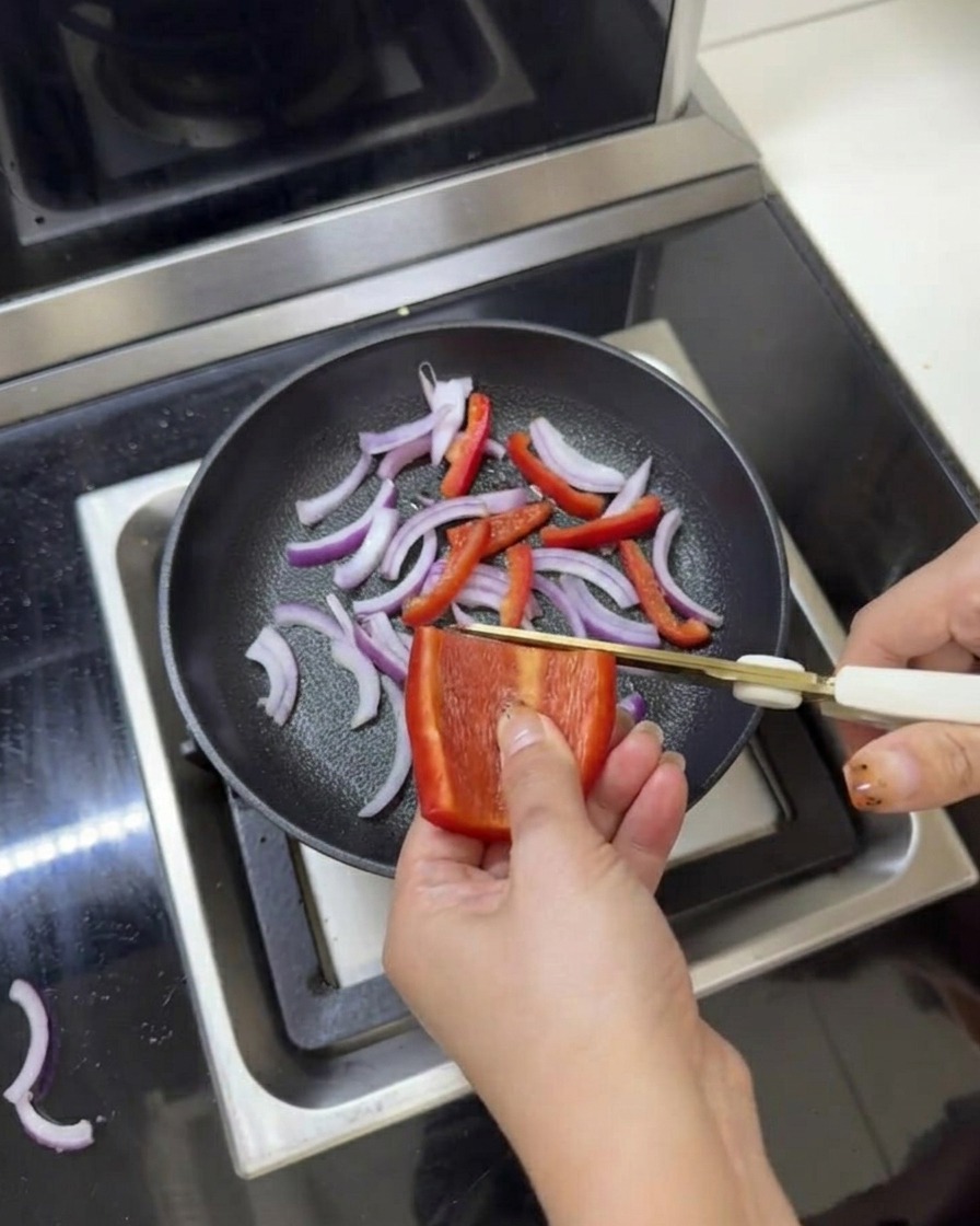 Geschnittene rote Zwiebeln und Paprika in einer Pfanne, gewürzt mit Salz und Pfeffer unter Verwendung von Küchenscheren.