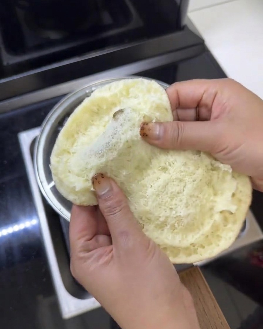 Frische grüne Salatblätter werden in ein geöffnetes Butter-Burger-Brötchen gelegt.