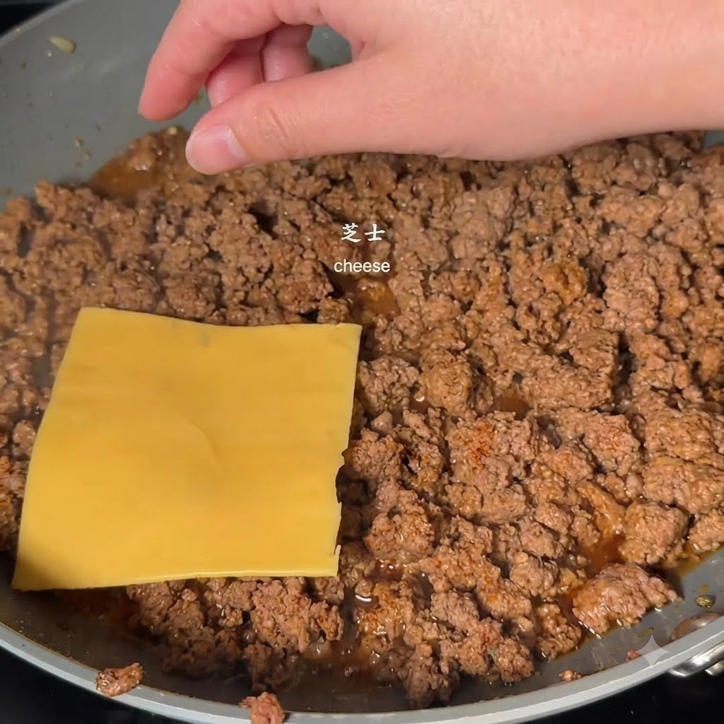 Eine gelbe Käsescheibe wird von einer Hand auf gekochtes Hackfleisch in einer Pfanne gelegt.