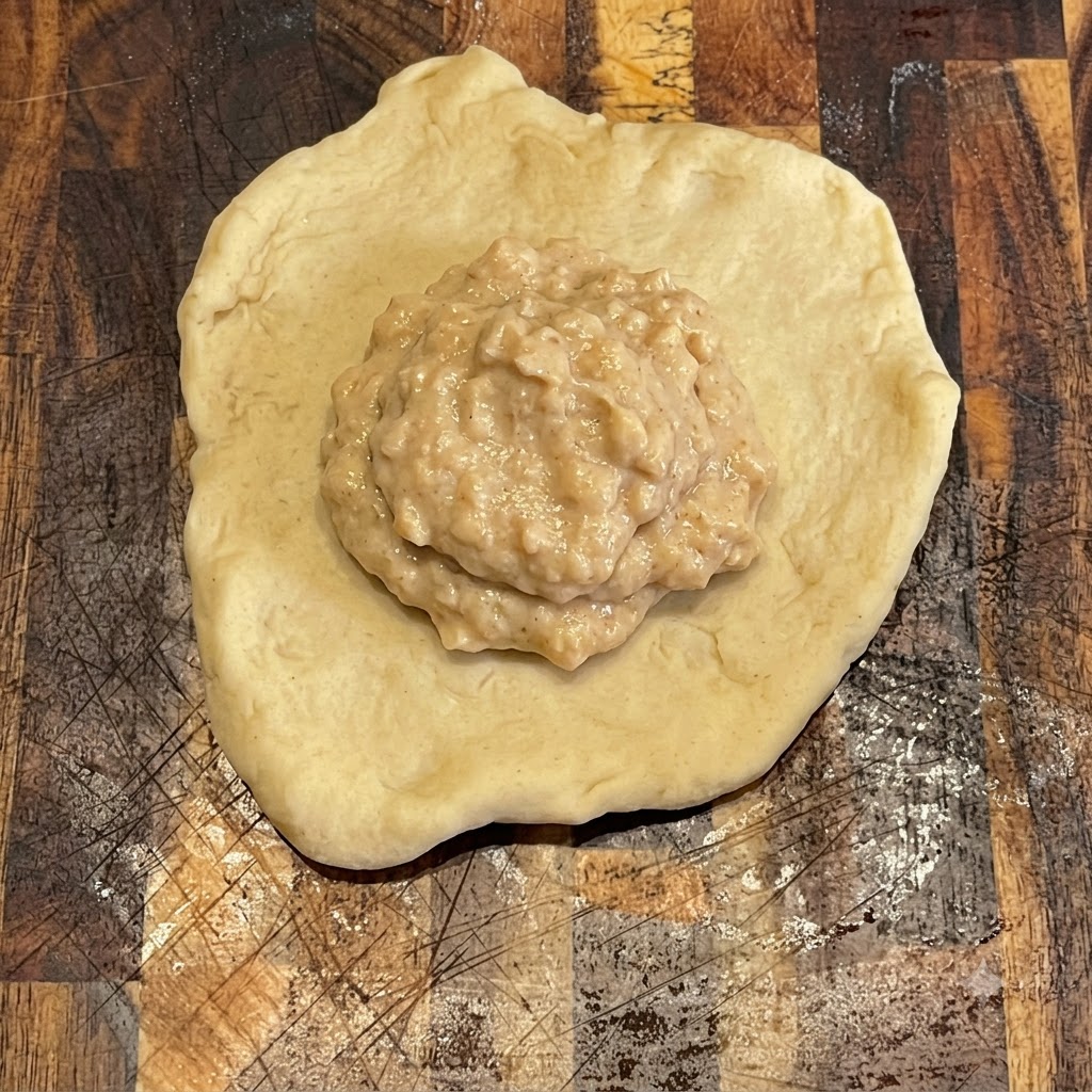 Burgersauce wird ordentlich auf einem flachen, runden Teigstück auf einem Holzbrett verteilt.
