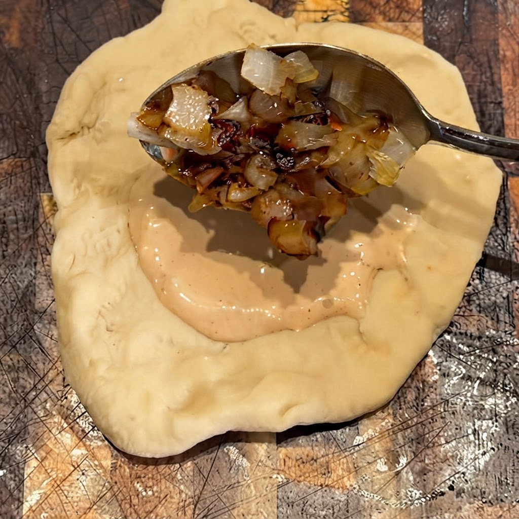 Gegrillte Zwiebeln werden auf die Saucenschicht auf dem Teig gelöffelt.