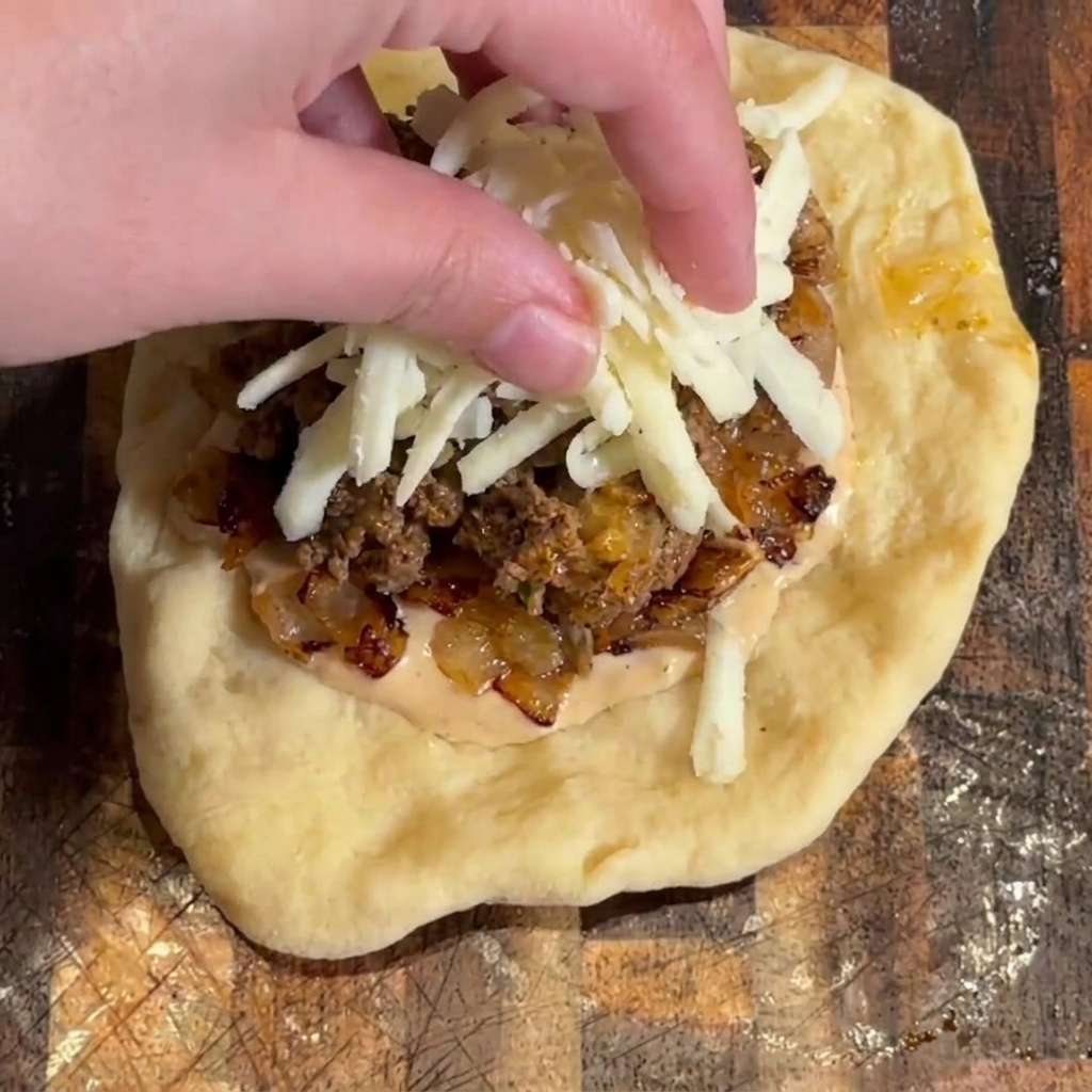 Geriebener Mozzarellakäse wird auf die Burgerfüllung gestreut.