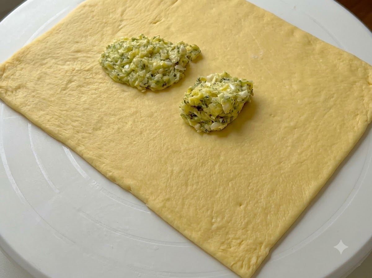 Häufchen aus grüner Knoblauchbutter liegen auf dem ausgerollten Teigrechteck.