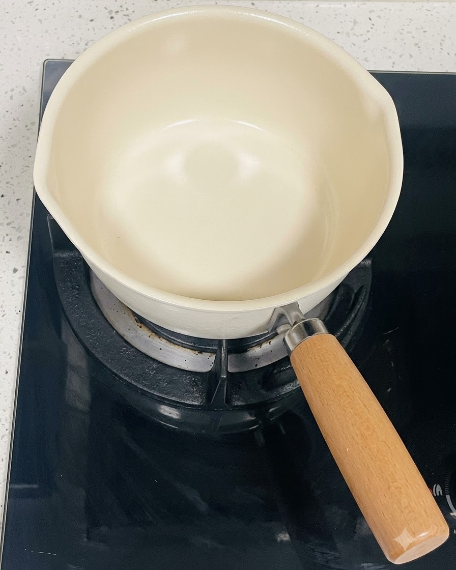 Ein leerer, cremefarbener Kochtopf auf einer schwarzen Induktionskochplatte.