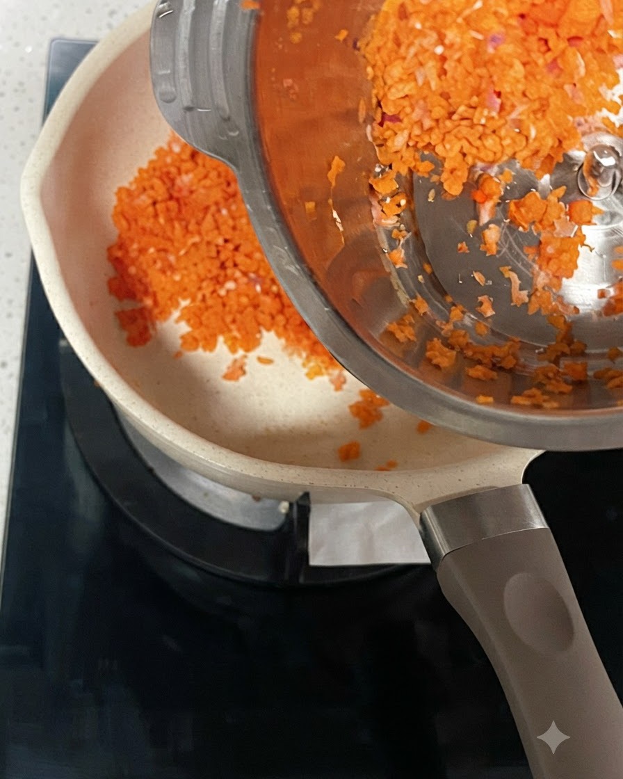 Fein gehackte Karotten und Zwiebeln werden aus einem Edelstahlbehälter in einen heißen Topf gegeben.