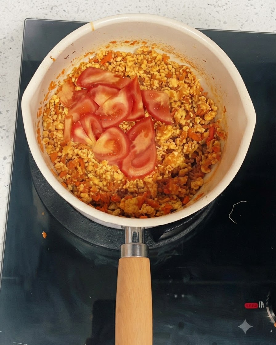 Frische Tomatenscheiben liegen auf der gekochten Hähnchen-Gemüse-Mischung in einer Pfanne.