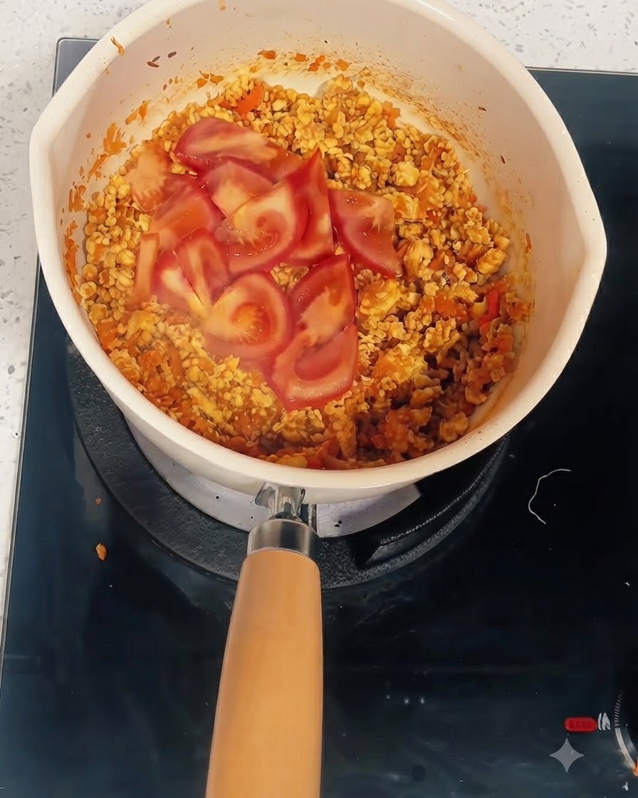 Tomatenscheiben über der gekochten Mischung in einem Topf, in den Wasser und Tomatenmark gegeben werden.