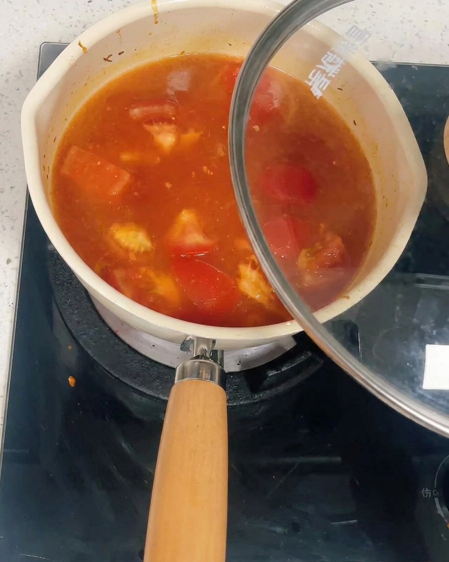 Ein mit Tomaten- und Hähnchensoße gefüllter Topf wird mit einem Glasdeckel abgedeckt.
