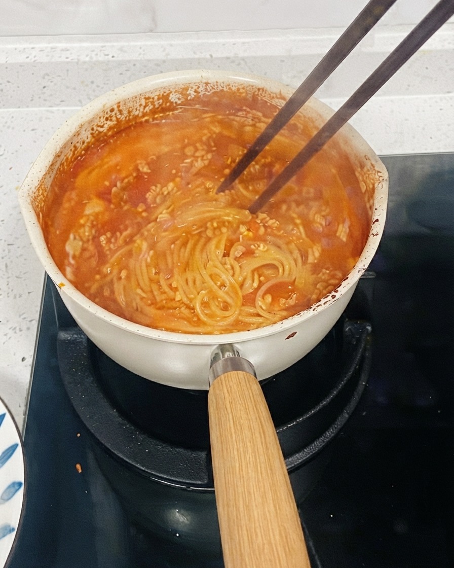 Ein Topf mit Tomatenpasta köchelt auf dem Herd, während Stäbchen die Nudeln umrühren, um die Soße einzudicken.