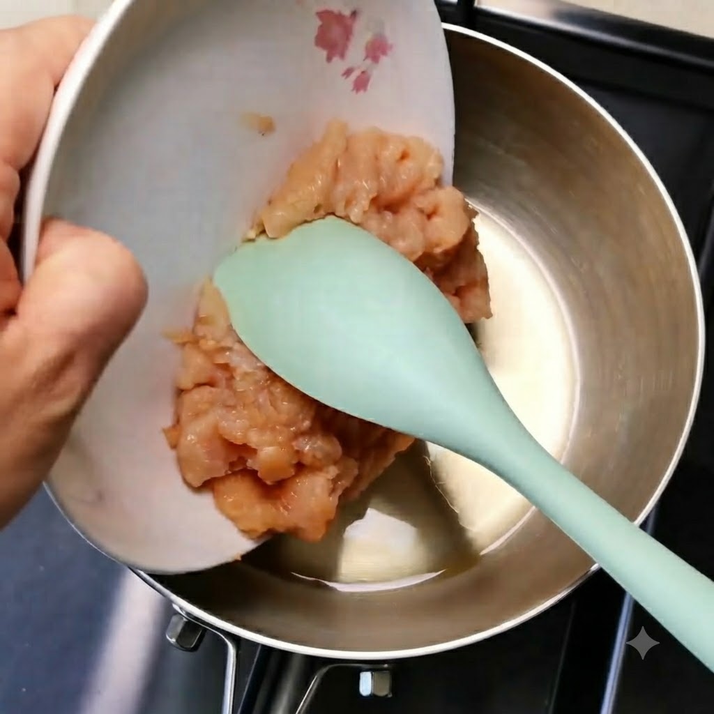 Hähnchenhackfleisch gleitet von einem weißen Teller mithilfe eines grünen Spatels in eine Metallpfanne.