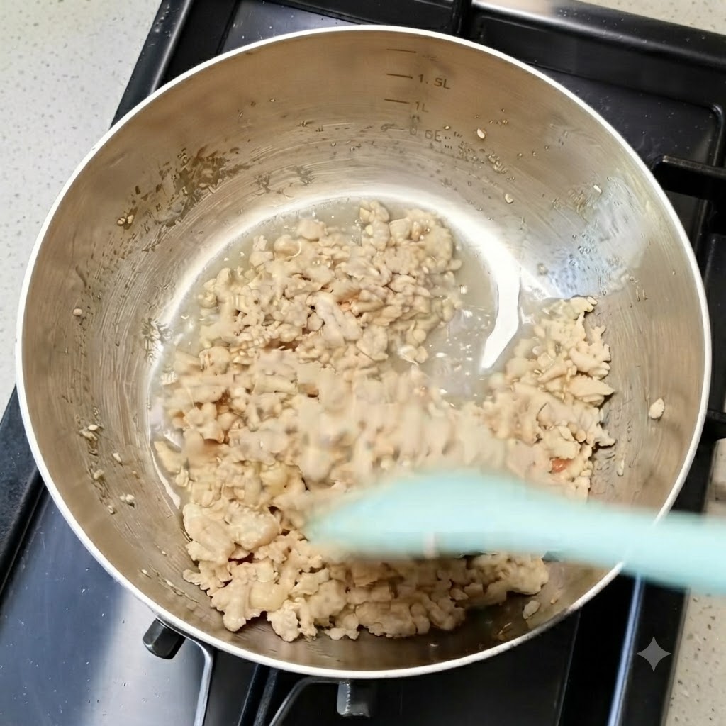 Gegartes Hähnchenhackfleisch wird in einer Metallpfanne mit einem grünen Spatel umgerührt.