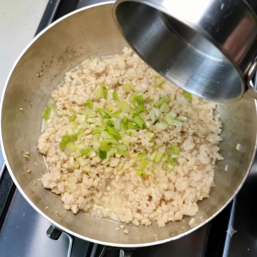 Gehackte Frühlingszwiebeln und Knoblauch verteilt auf dem gebratenen Hackfleisch in einer Pfanne.