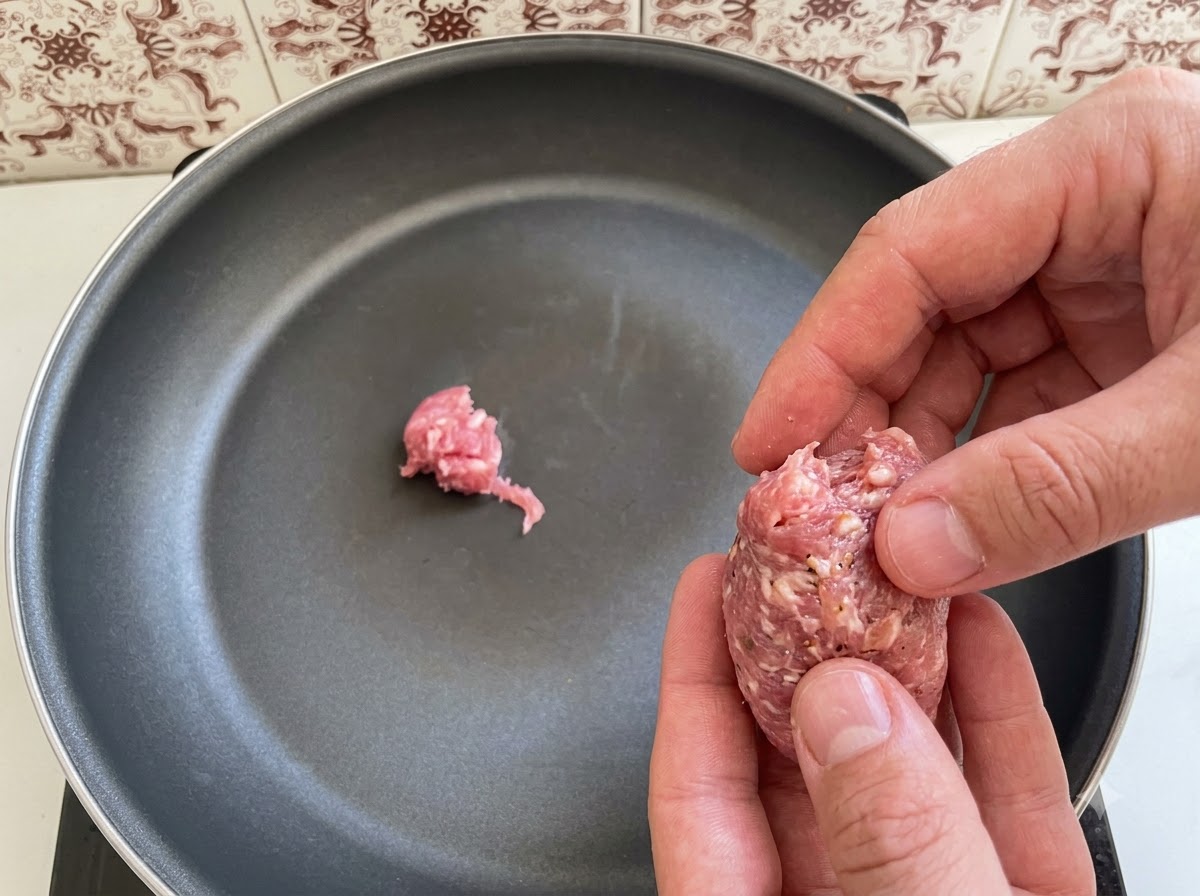 Stücke von italienischem Bratwurstbrät werden in einer Bratpfanne arrangiert und hineingegeben.