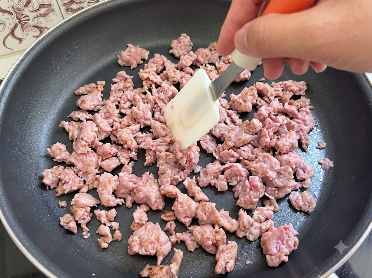 Italienisches Bratwurstbrät wird mit einem Spatel in einer Pfanne aktiv umgerührt und gebraten.