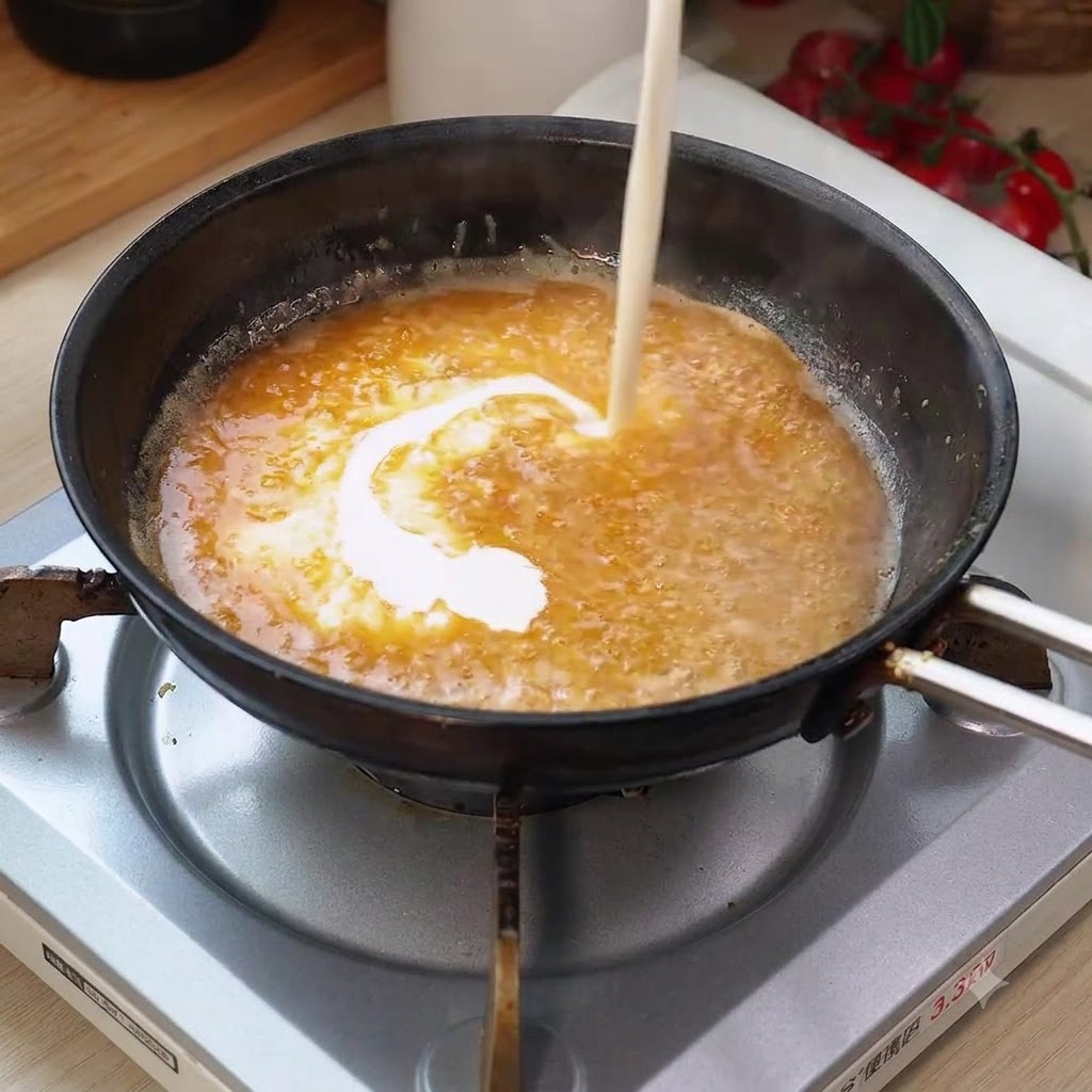 Schlagsahne wird in die brodelnde Pfannensauce gegossen und erzeugt eine wirbelnde Mischung.