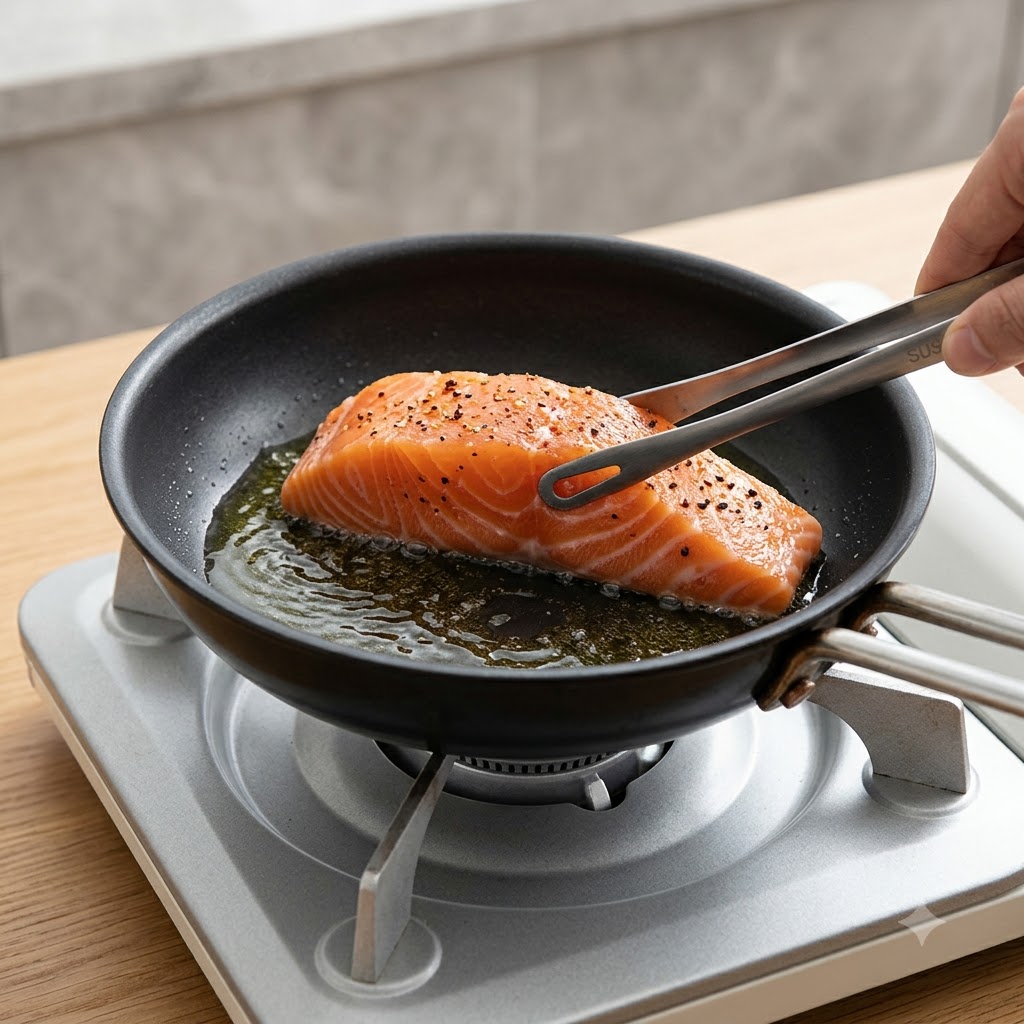 Ein frisches Lachsfilet wird mit einer Küchenzange mit der Hautseite nach unten in eine heiße Bratpfanne gelegt.