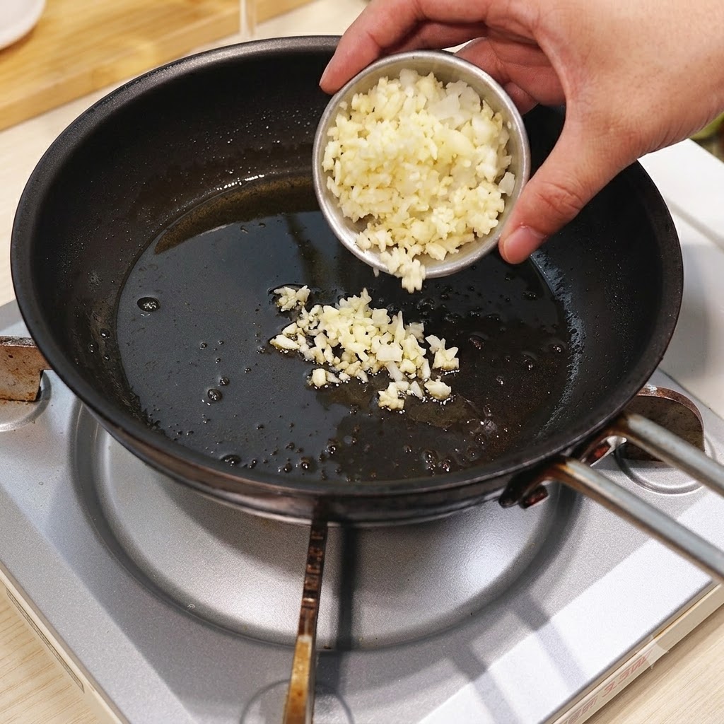 Gehackter Knoblauch und Zwiebeln werden aus einer kleinen Schüssel in eine heiße Bratpfanne mit Öl gegeben.