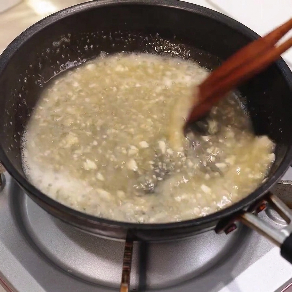 Butter schmilzt in einer brodelnden Pfannensauce und wird mit Holzstäbchen verrührt.