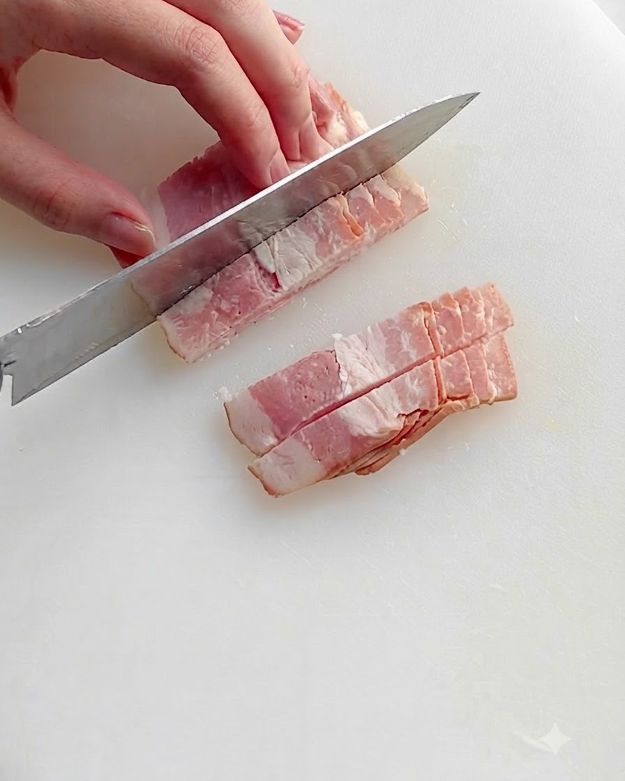 Gehackte Speckstücke braten in einer heißen Pfanne mit Öl, was brutzelndes Fett und bräunende Ränder zeigt.