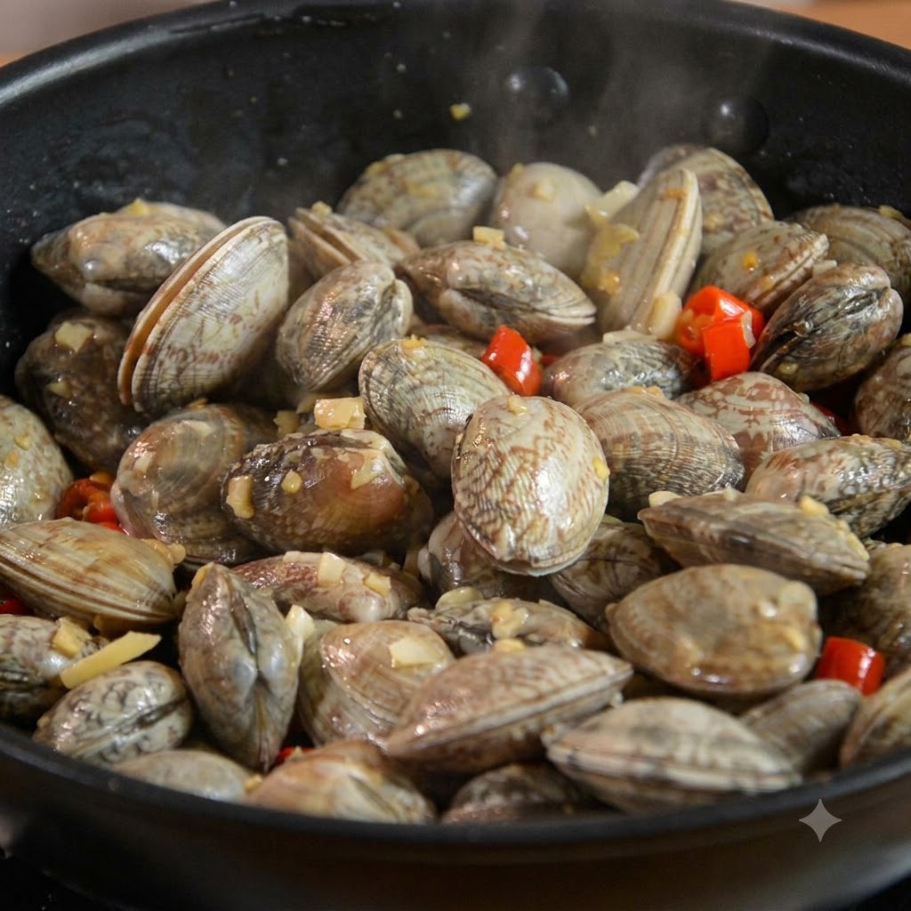 Muscheln vermischt mit Knoblauch und Chili in einer schwarzen Pfanne.