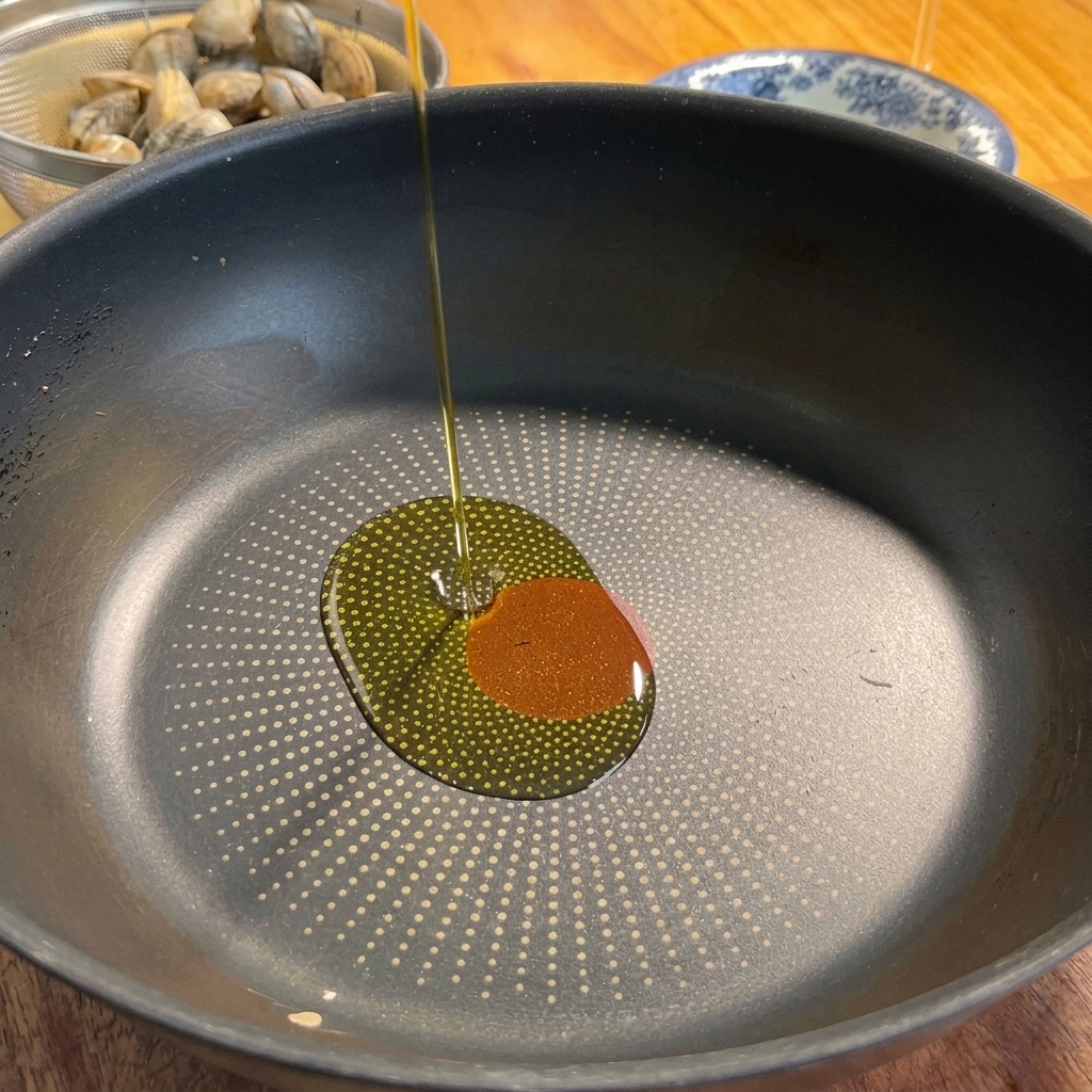 Olivenöl wird in eine Pfanne gegossen, zusammen mit Knoblauch und Chilischote.