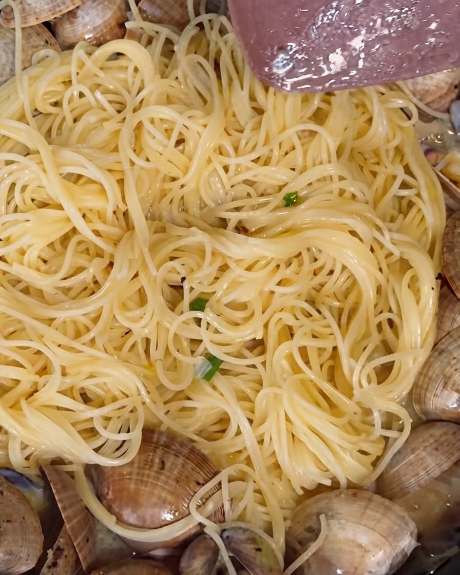 Weißer Pfeffer in Pulverform und frisch gemahlener schwarzer Pfeffer werden über köchelnden Muscheln in einer Pfanne verstreut.