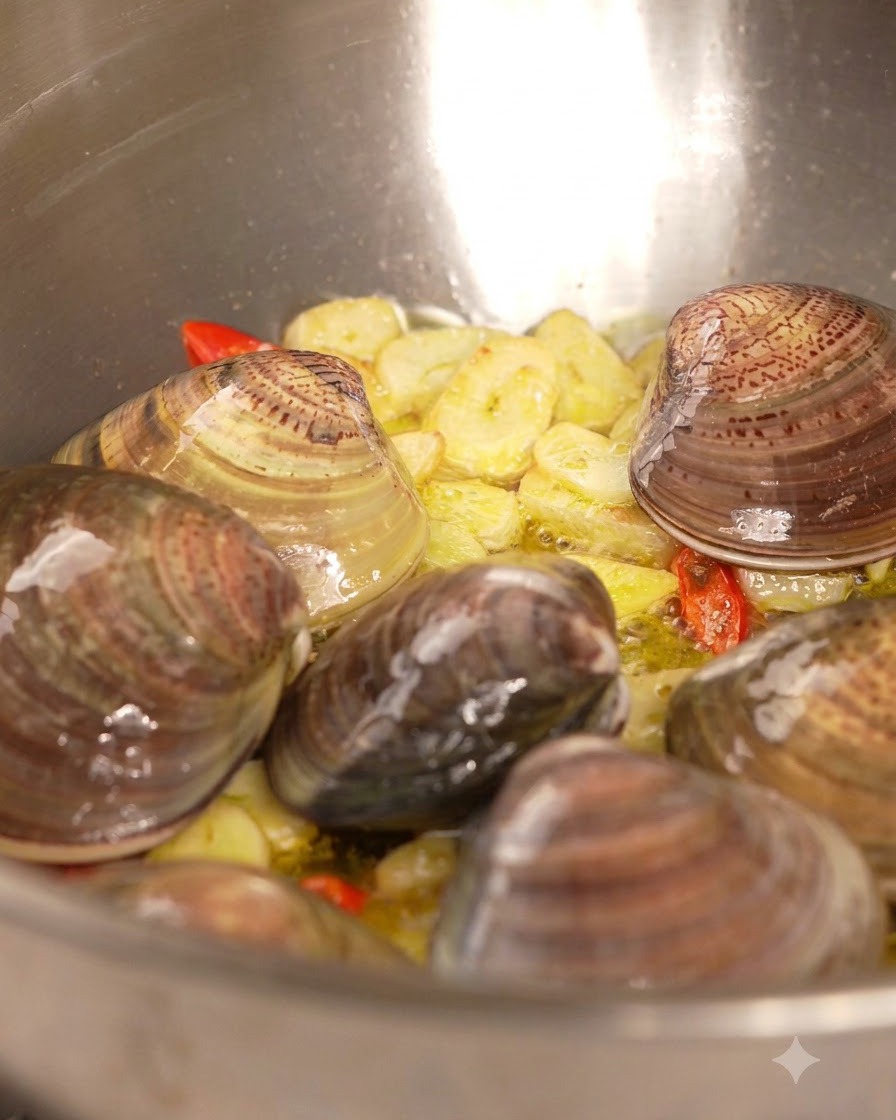Weißwein wird aus einer Flasche in eine mit Muscheln, Knoblauch und Chili gefüllte Pfanne gegossen.