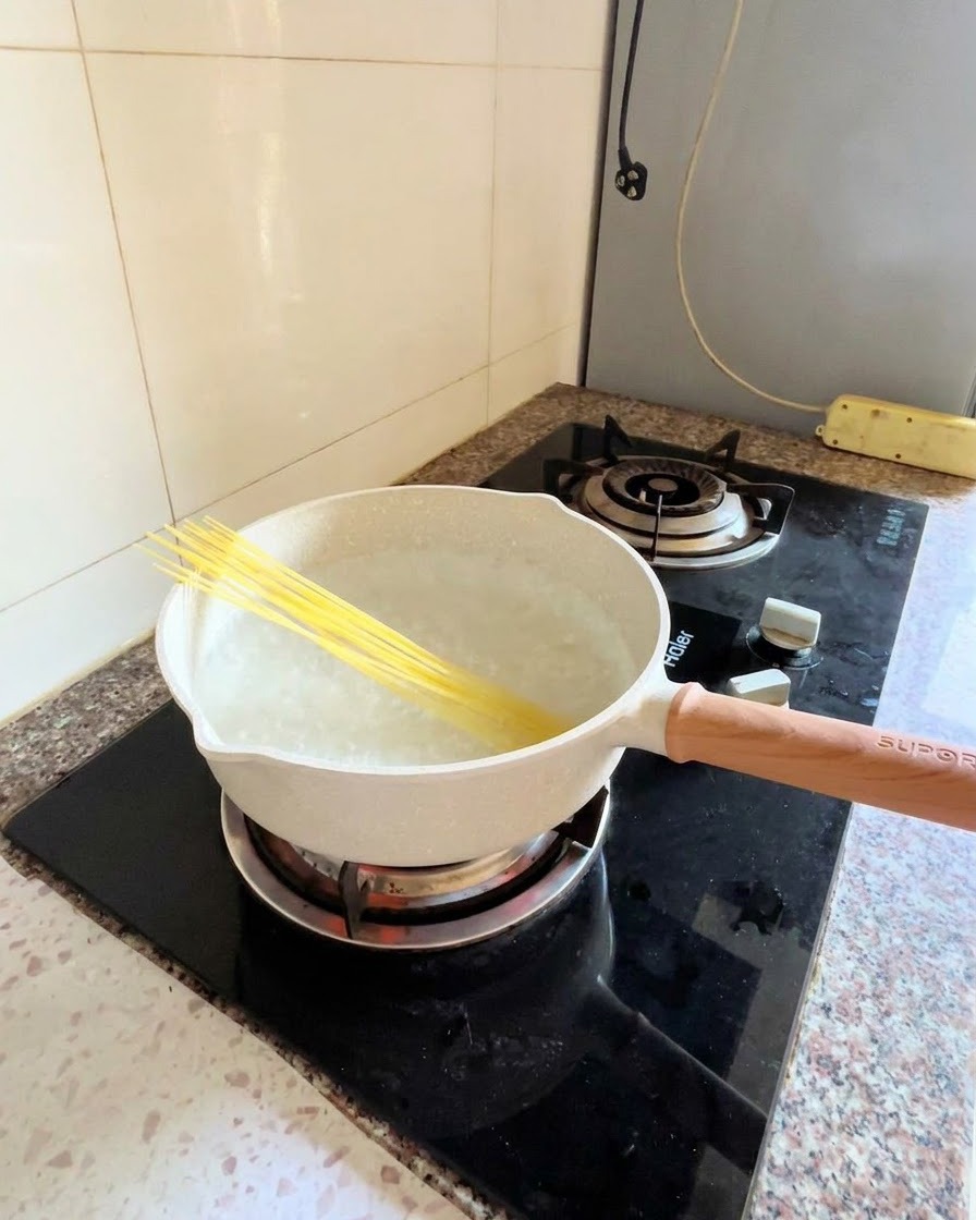 Trockene Spaghettinudeln diagonal in einem Topf mit kochendem Wasser auf einem Herd.