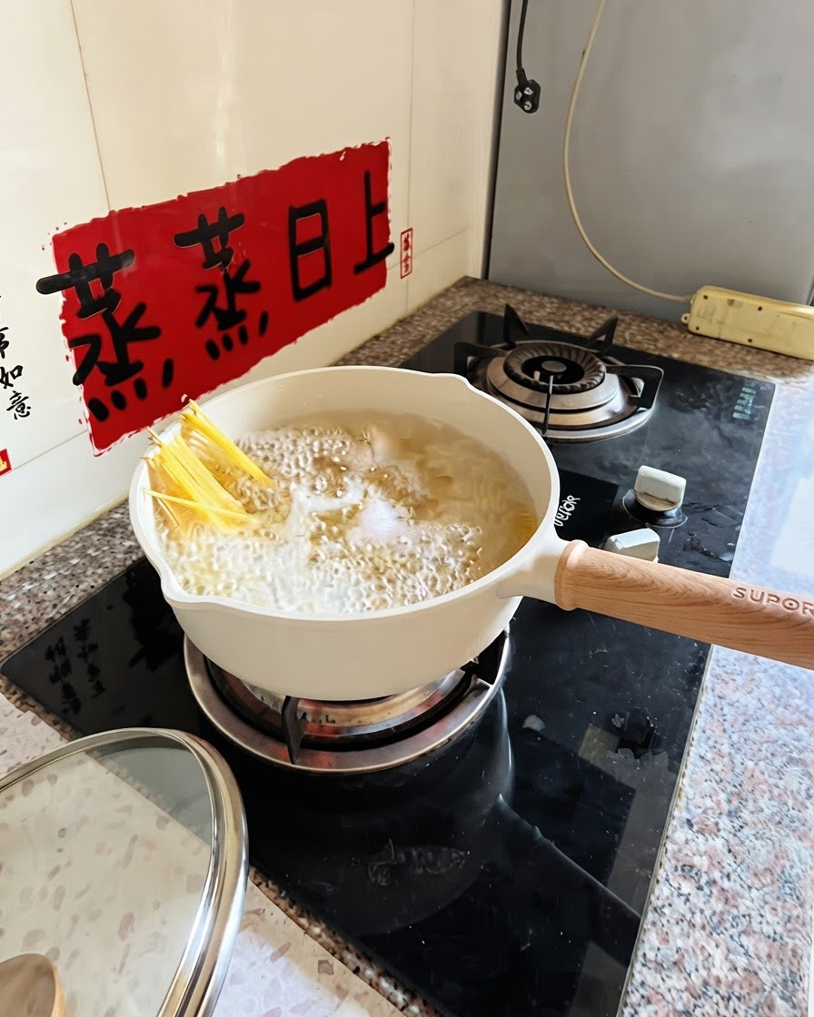 Spaghetti kochen in einem weißen Topf, während eine Zange die Nudeln teilweise untertaucht.