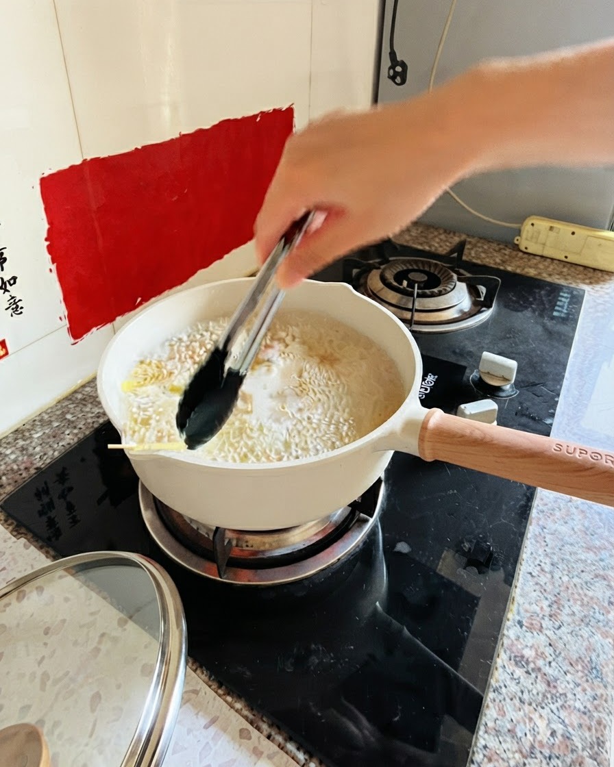Zange rührt Pasta in einem Topf mit kochendem Wasser auf dem Herd um.