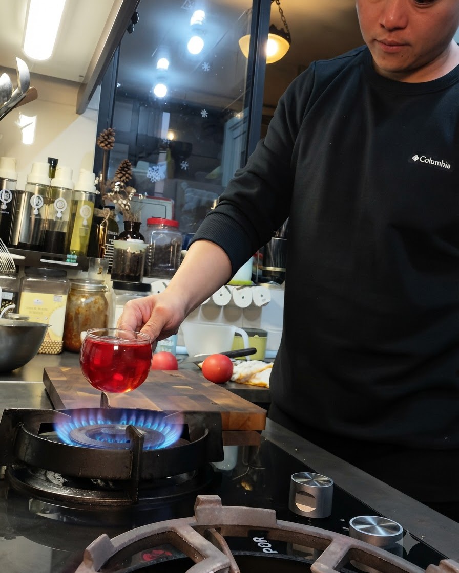 Eine Tomate wird über die blaue Flamme eines Gasherds gehalten, die Oberfläche ist kreuzweise eingeritzt.