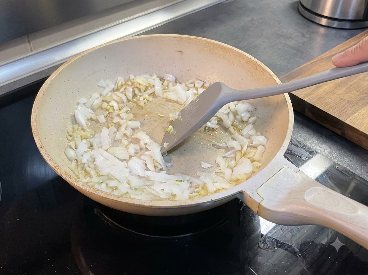 Gehackte Zwiebeln werden mit einem Pfannenwender in der zerlassenen Butter in einer Pfanne verrührt.