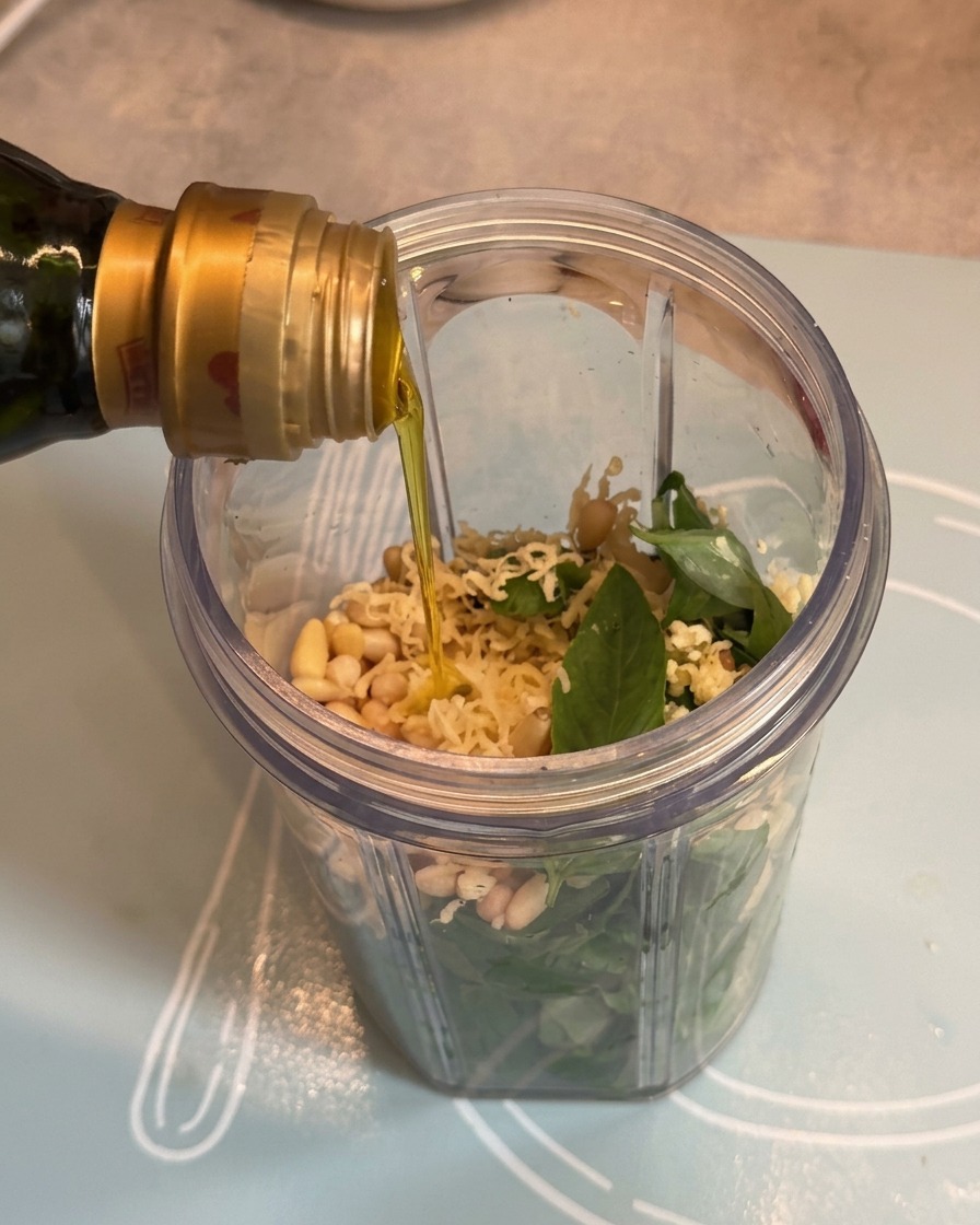 Olivenöl wird aus einer Flasche über die Pesto-Zutaten in den Mixbecher gegossen.