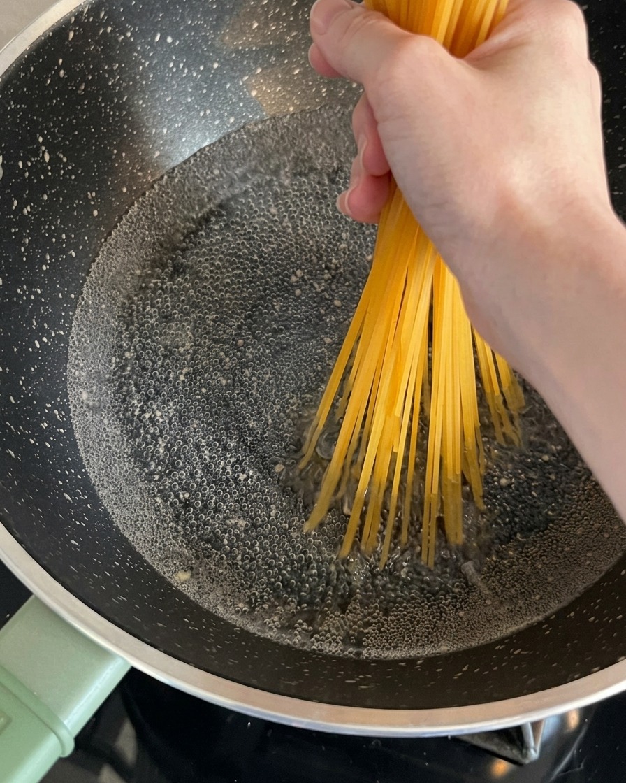 Trockene Spaghetti-Nudeln werden von einer Hand gehalten und in einen sprudelnden Topf mit Wasser gegeben.