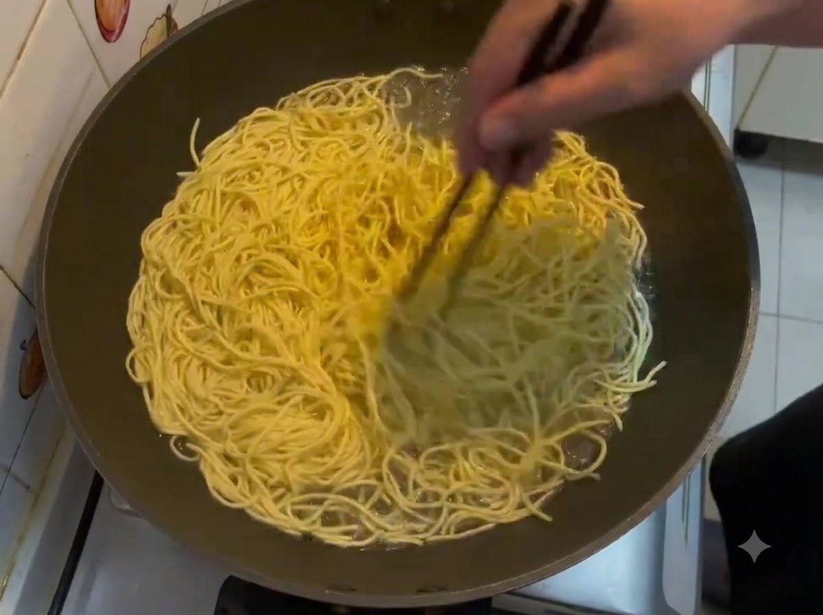 Stäbchen rühren eine große Menge gelber E-Fu-Nudeln um, die in einem Wok kochen.