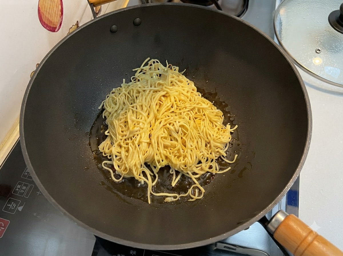 Abgetropfte E-Fu-Nudeln werden in einem schwarzen Wok mit einem Pfannenwender pfannengerührt.