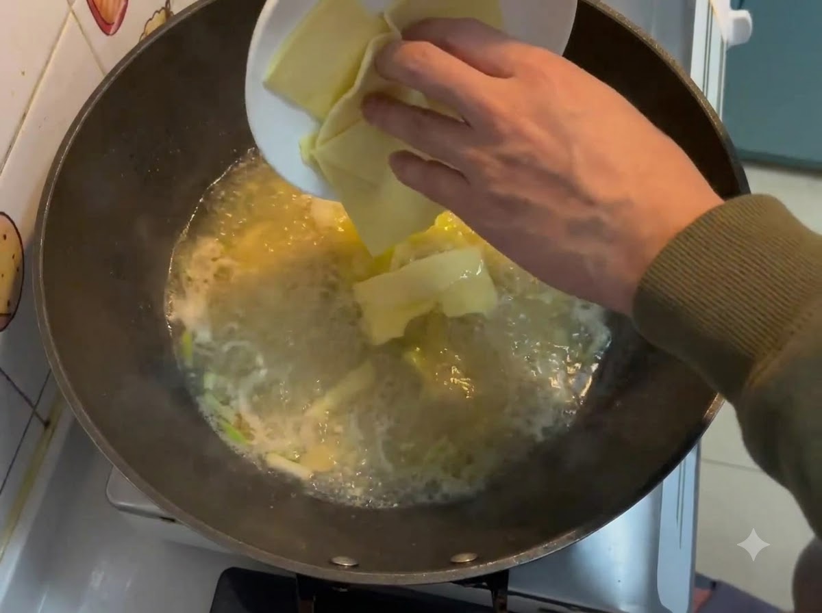 Quadratische Käsescheiben werden von einem weißen Teller in eine sprudelnde cremige Brühe in einem Wok fallengelassen.