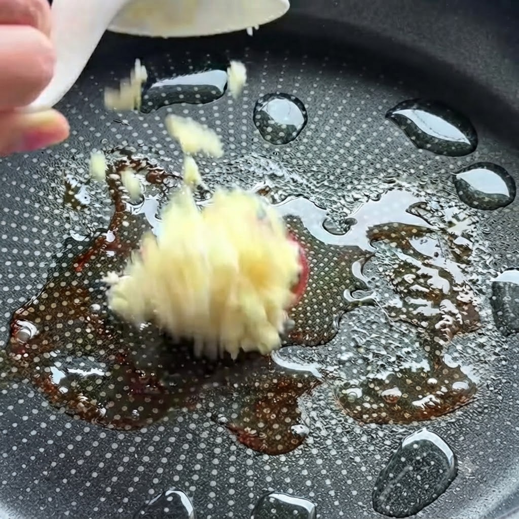 Fein gehackter Knoblauch wird in eine heiße Bratpfanne mit Öl gegeben.
