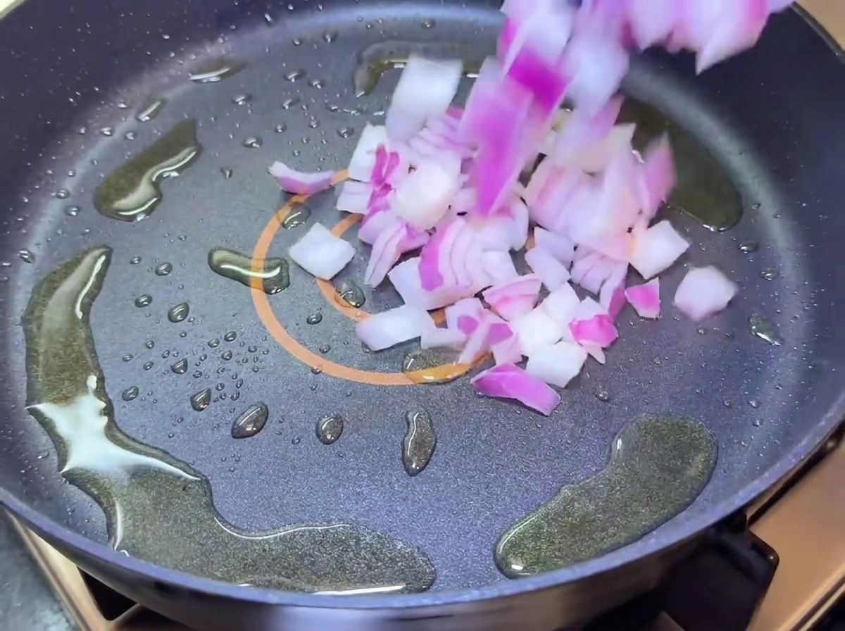 Gewürfelte rote Zwiebeln fallen in eine Bratpfanne mit Öl.