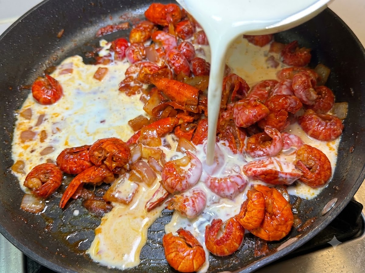 Milch und Schlagsahne werden aus einer Schüssel in die Pfanne mit Krebsfleisch und Zwiebeln gegossen.