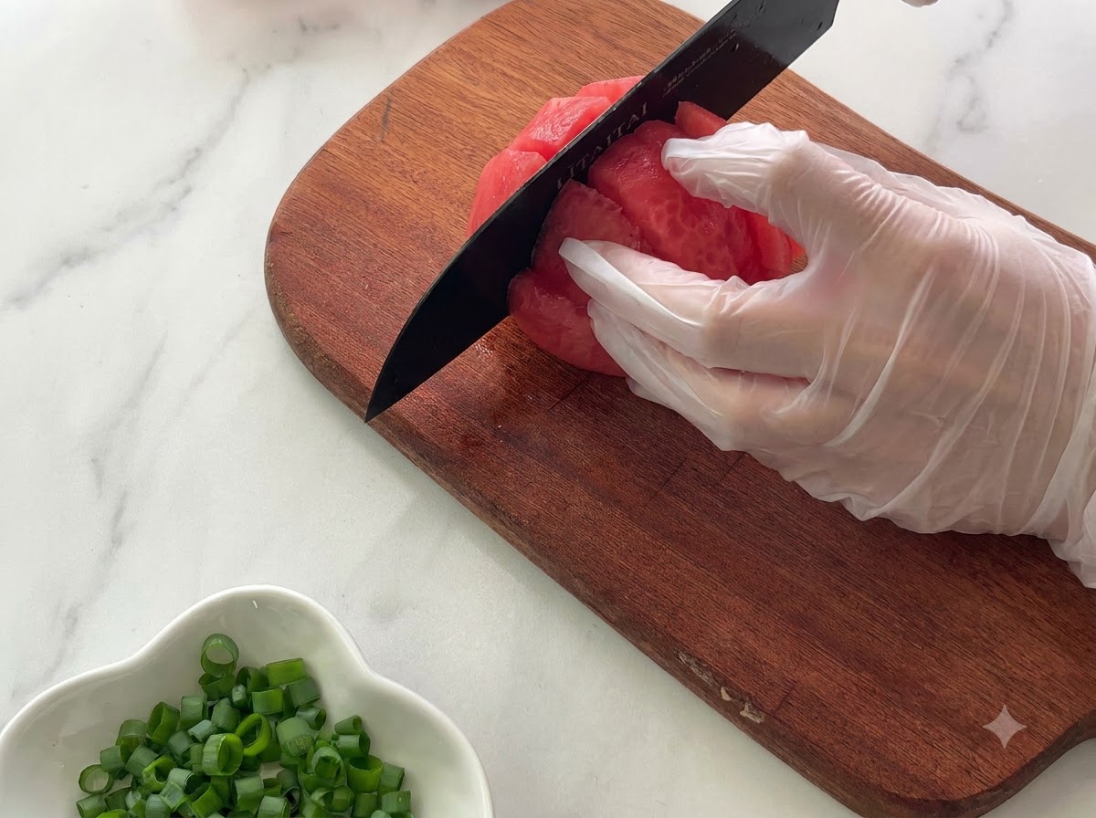 Eine bemalte Hand hält eine Tomate auf einem Holzschneidebrett, während sie mit einem schwarzen Messer in Stücke geschnitten wird.